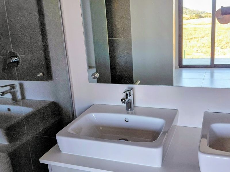 Modern bathroom featuring a double vanity with vessel sinks, chrome fixtures, and large wall mirror, with stone tiling and glass shower enclosure.