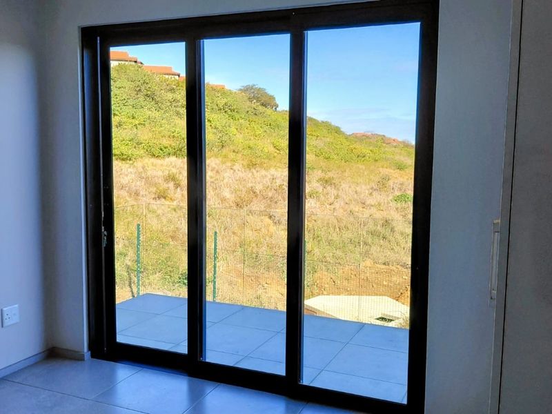 Bright living area featuring large sliding glass doors that open onto a tiled patio with scenic hillside views.