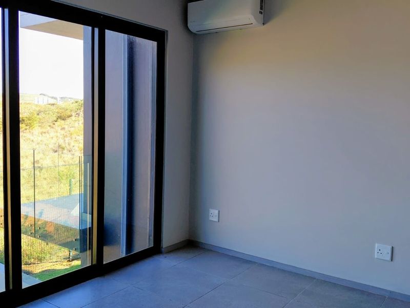 Modern bedroom featuring tiled flooring, a wall-mounted air conditioning unit, and large sliding glass doors providing natural light and access to the outdoors.