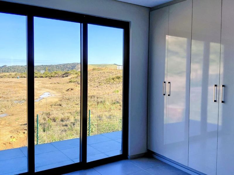 Modern bedroom featuring sleek built-in cupboards, large sliding glass doors, and expansive views of the surrounding landscape.