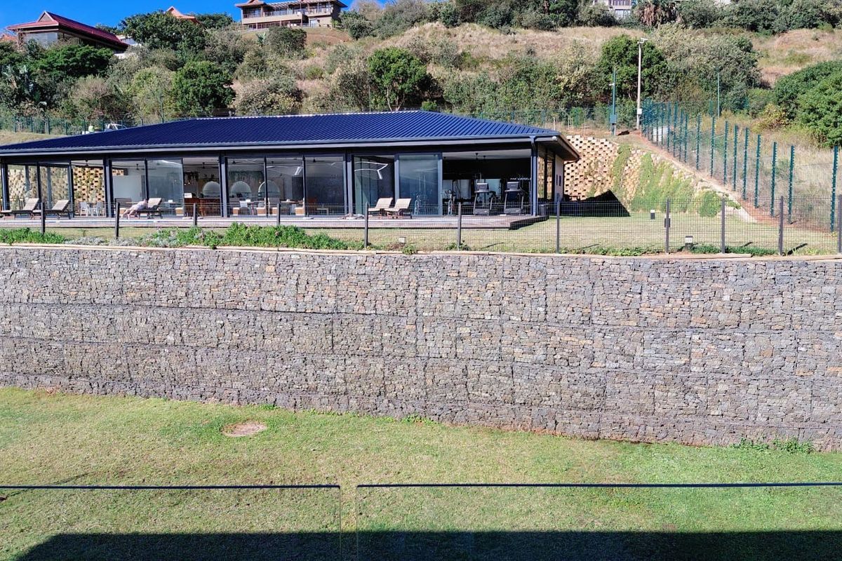 Rear view of a modern property featuring a large timber deck, extensive sliding glass doors, and a prominent stone gabion retaining wall.