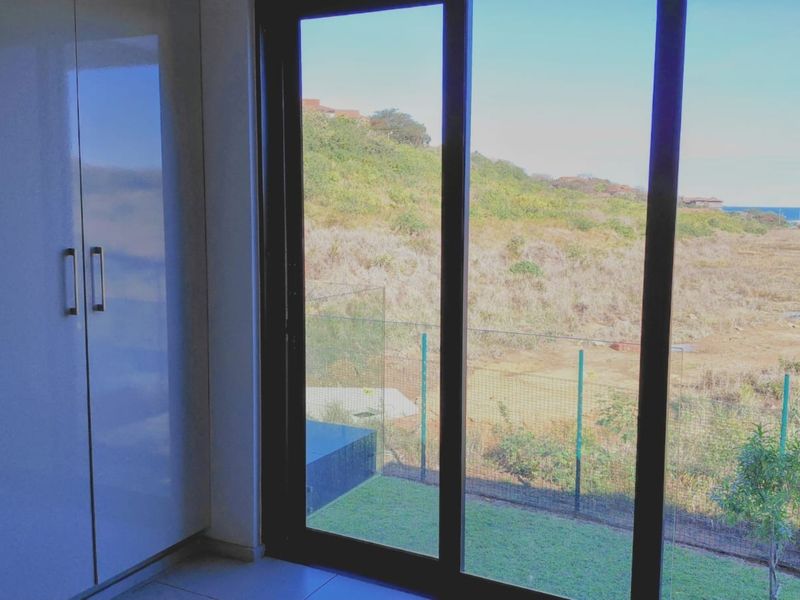 A bright bedroom featuring modern built-in cupboards, tiled flooring, and large sliding glass doors that open to a scenic outdoor view.