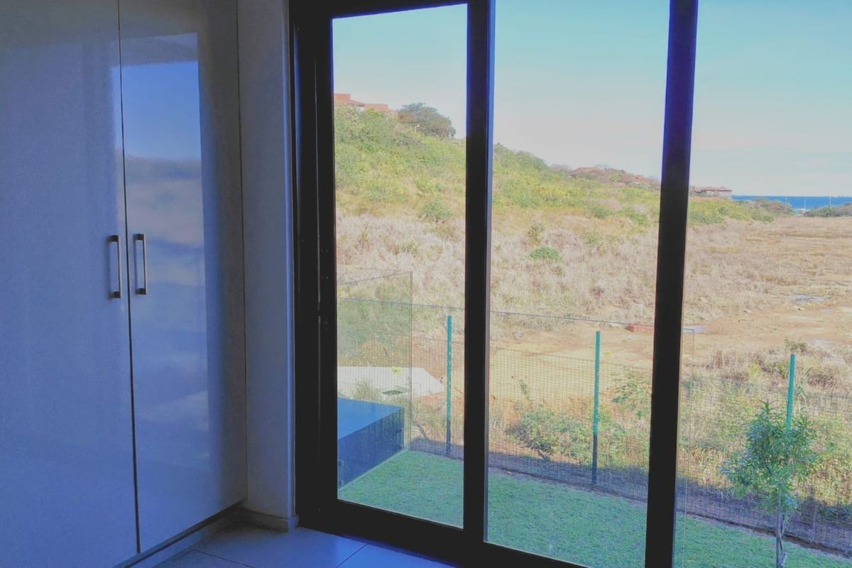 A bright bedroom featuring modern built-in cupboards, tiled flooring, and large sliding glass doors that open to a scenic outdoor view.