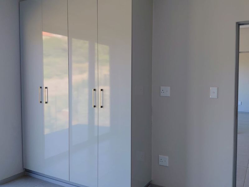 A bright, modern bedroom featuring high-gloss built-in cupboards, neutral tiled flooring, and a sliding glass door providing natural light and outdoor access.
