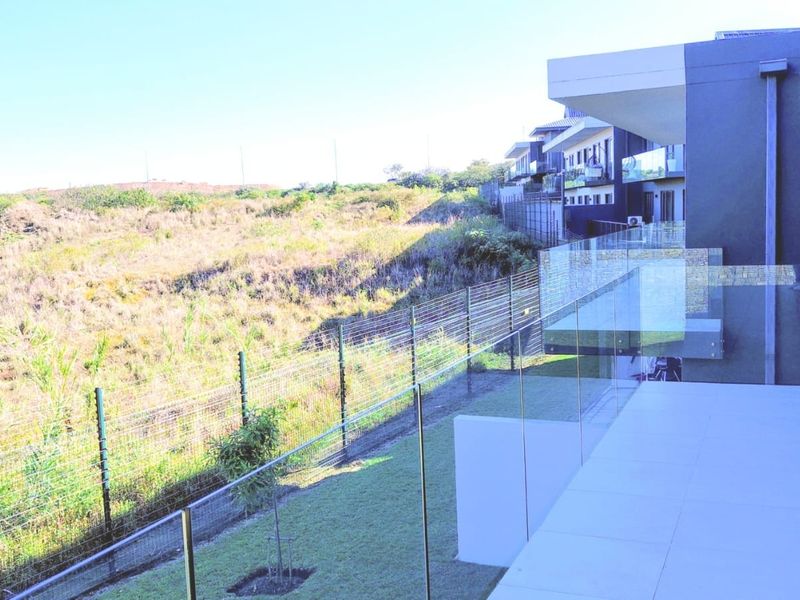 Modern balcony featuring a sleek glass balustrade, tiled flooring, and direct access to the living area, overlooking an open landscape.