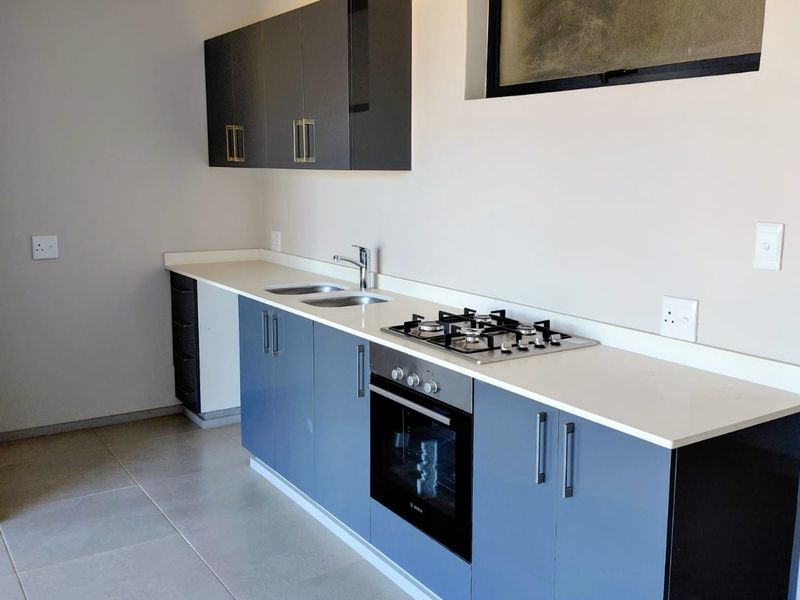 Modern kitchen featuring sleek blue cabinetry, stone countertops, a built-in gas hob, and an integrated oven with neutral tiled flooring.