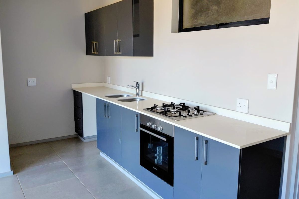 Modern kitchen featuring sleek blue cabinetry, stone countertops, a built-in gas hob, and an integrated oven with neutral tiled flooring.