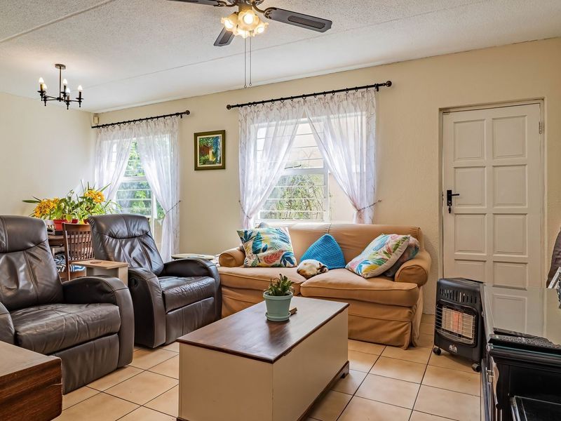 A comfortable living room featuring tiled flooring, a ceiling fan, and large windows with security bars, providing a functional and well-lit space.