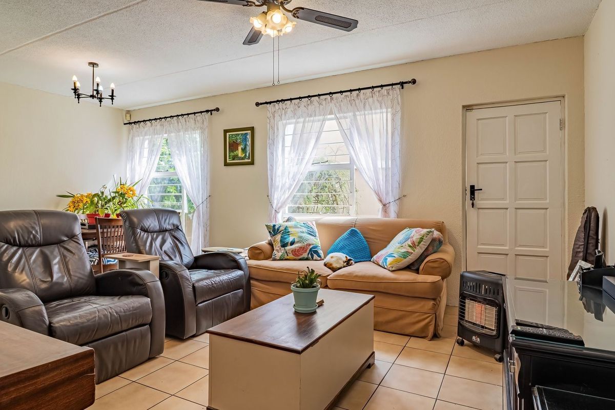A comfortable living room featuring tiled flooring, a ceiling fan, and large windows with security bars, providing a functional and well-lit space.