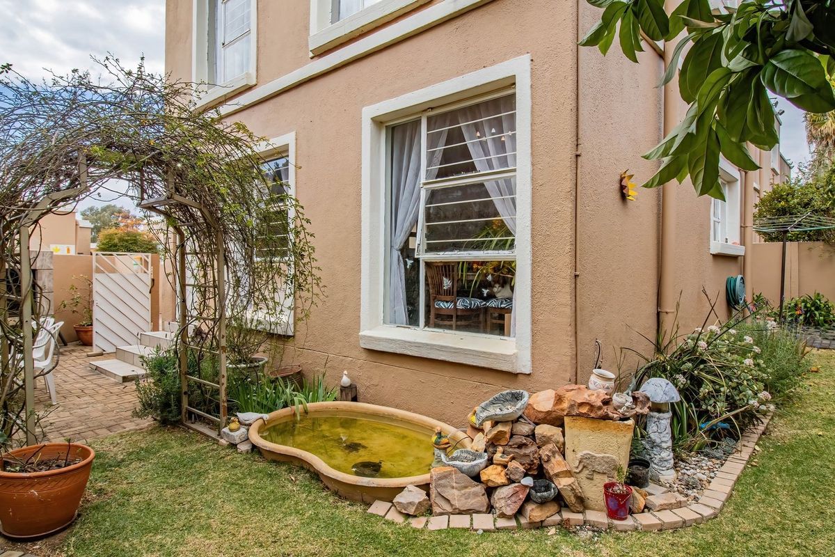 Rear exterior view of the townhouse featuring a small garden, paved patio area, and security bars on the windows.