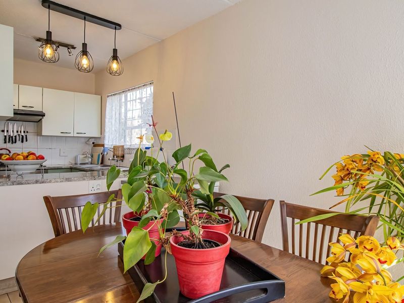 An open-plan dining area adjacent to a functional kitchen featuring white cabinetry, granite countertops, and modern pendant lighting.