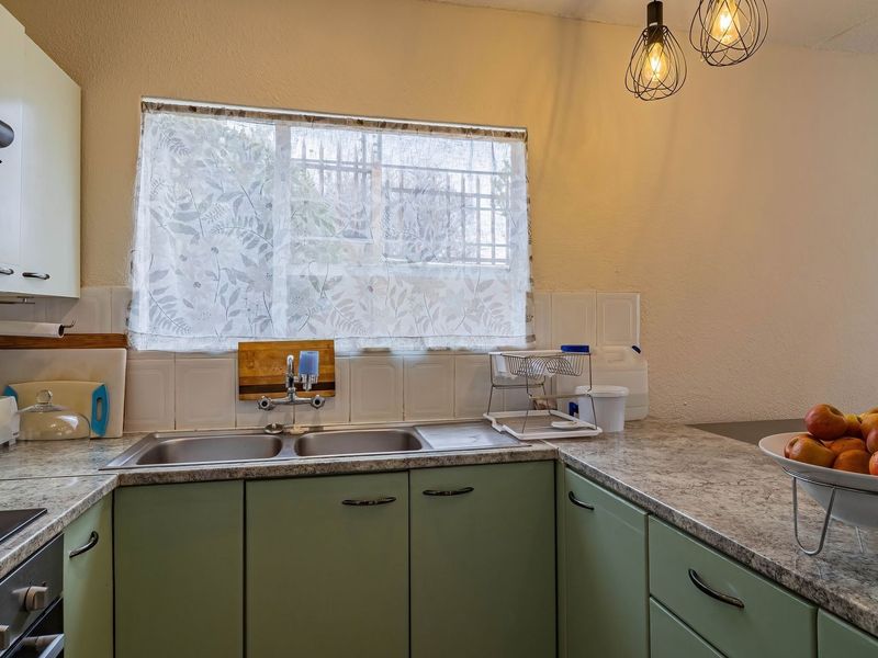 A functional kitchen featuring green cabinetry, laminate countertops, a double bowl sink, and a built-in hob with an extractor fan.