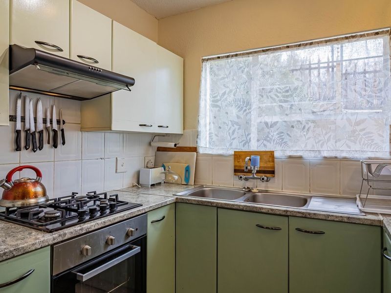 A functional kitchen featuring built-in cabinetry, a gas hob with extractor fan, and a double bowl stainless steel sink with tiled backsplash.