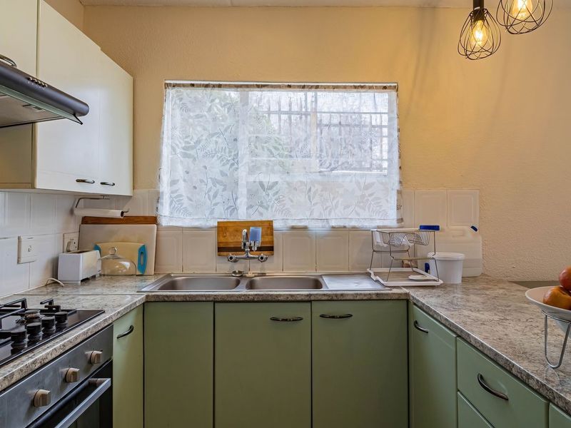 A functional kitchen featuring fitted cabinetry, a gas hob with extractor fan, double basin sink, and laminate countertops with a tiled backsplash.