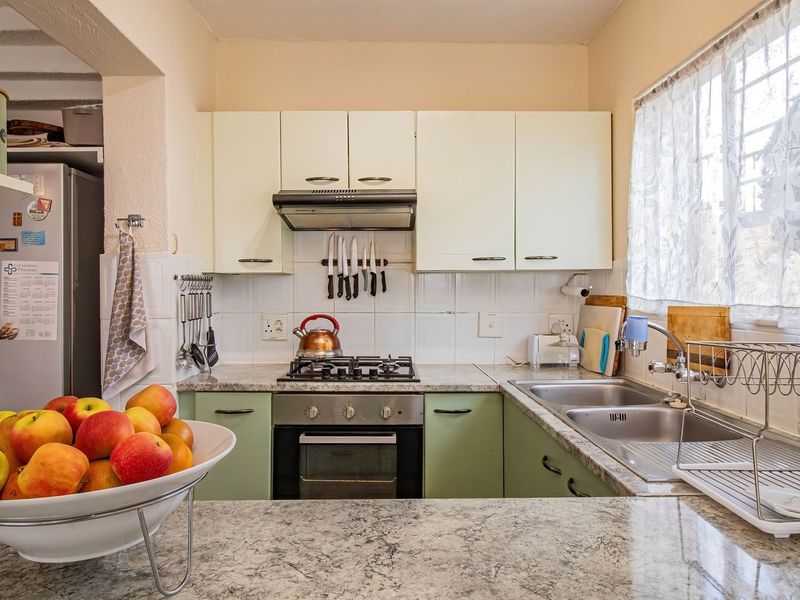 A functional kitchen featuring granite countertops, built-in cabinetry, a gas hob, and a stainless steel double sink with a window view.