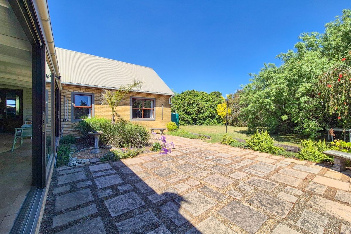 A spacious rear exterior featuring a paved patio area, brick facade, and a well-maintained garden with mature trees.