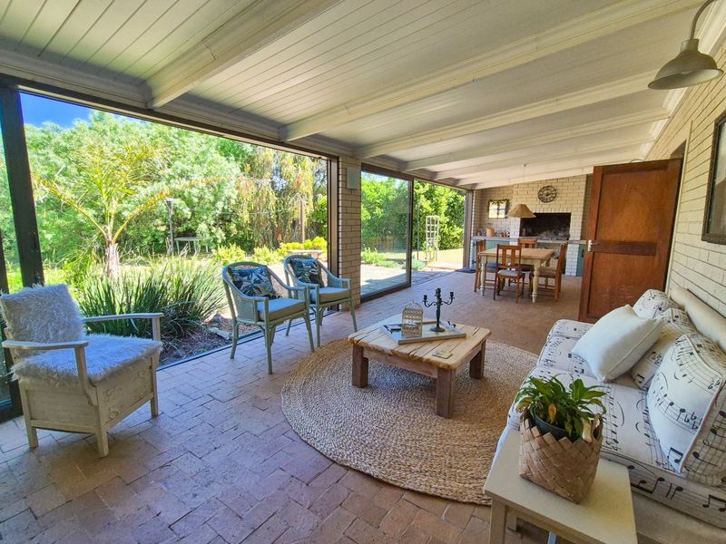 Spacious covered patio featuring brick flooring, a built-in braai, and large sliding glass doors that open to the garden.