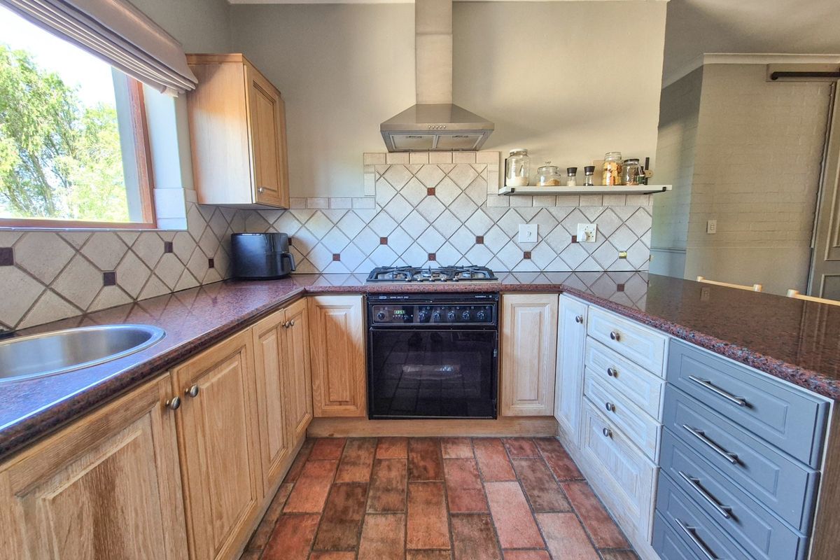 A functional kitchen featuring wooden cabinetry, granite countertops, a gas hob with extractor fan, and classic terracotta floor tiles.