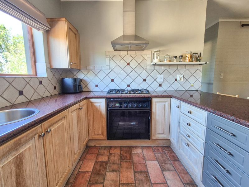 A functional kitchen featuring wooden cabinetry, granite countertops, a gas hob with extractor fan, and classic terracotta floor tiles.