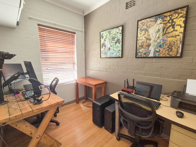 A functional home office featuring laminate flooring, painted brick walls, and an integrated air conditioning unit.