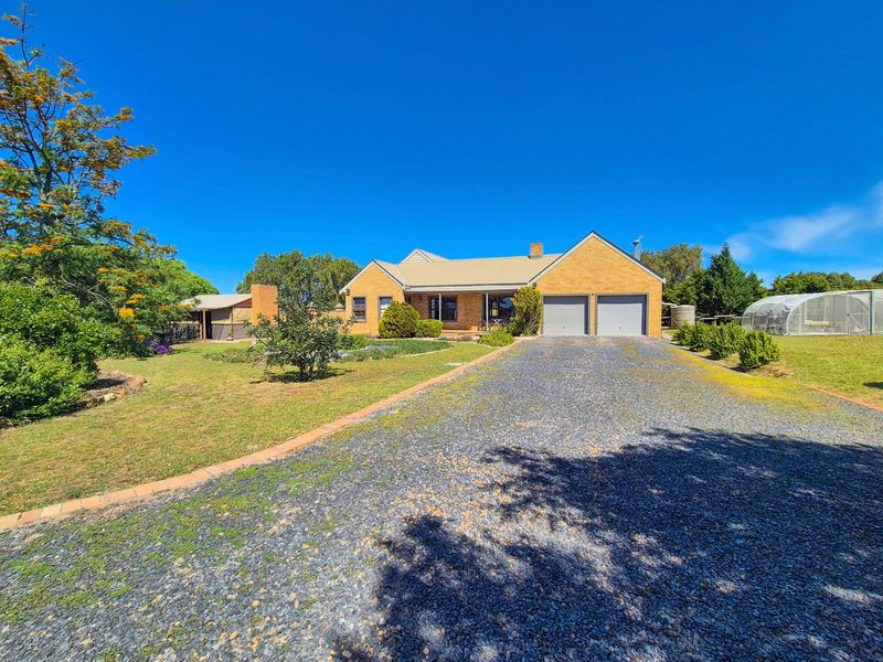 A single-story brick house featuring a double garage, a long gravel driveway, and a spacious front garden under a clear blue sky.