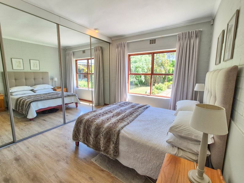 A well-lit bedroom featuring timber-look laminate flooring, painted brick walls, and large mirrored sliding wardrobe doors, offering a bright and comfortable living space.