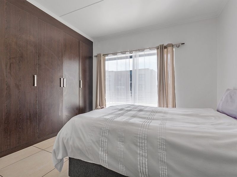 A well-maintained bedroom featuring dark wood built-in cupboards and neutral tiled flooring, offering a clean and functional living space.