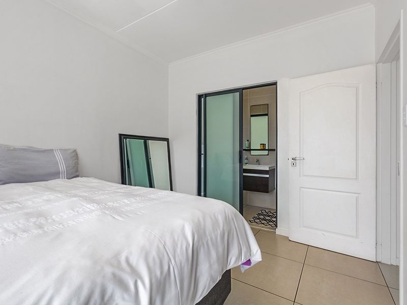 A clean bedroom featuring neutral tiled flooring and a sliding glass door providing access to an en-suite bathroom.