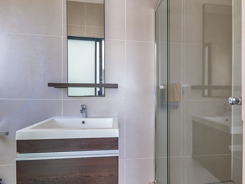 Modern bathroom featuring a dark wood vanity cabinet, basin with mixer tap, wall-mounted mirror, and a glass-enclosed shower with neutral wall tiling.