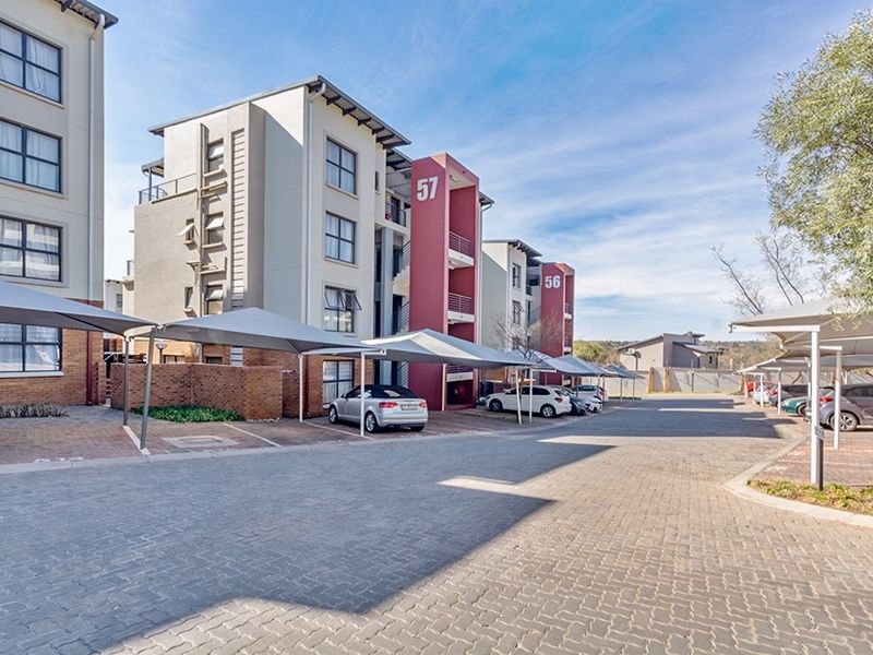 Exterior view of a modern multi-story apartment complex featuring paved parking areas and covered carports.