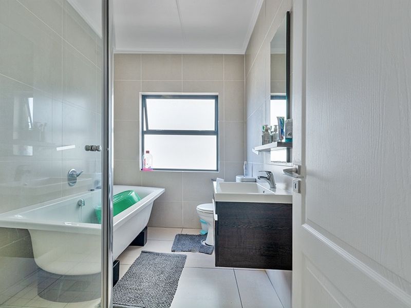 A clean, modern bathroom featuring a bathtub, wall-mounted vanity with basin, toilet, and neutral tiled finishes throughout.