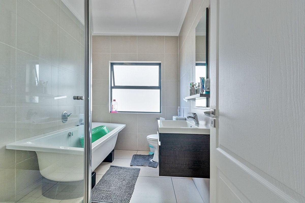 A clean, modern bathroom featuring a bathtub, wall-mounted vanity with basin, toilet, and neutral tiled finishes throughout.