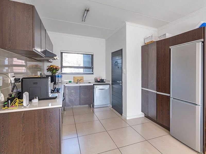 Functional kitchen featuring dark wood-look cabinetry, tiled flooring, a stainless steel sink, and a tiled backsplash with integrated extractor fan.