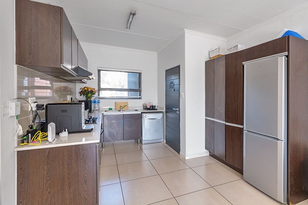 Functional kitchen featuring dark wood-look cabinetry, tiled flooring, a stainless steel sink, and a tiled backsplash with integrated extractor fan.