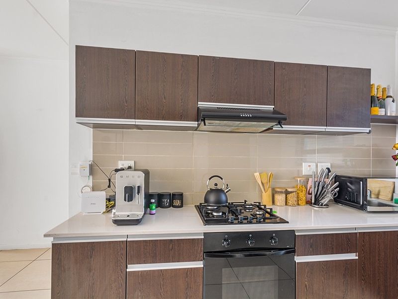 Modern kitchen featuring dark wood cabinetry, stone countertops, a gas hob with extractor fan, and a tiled backsplash.