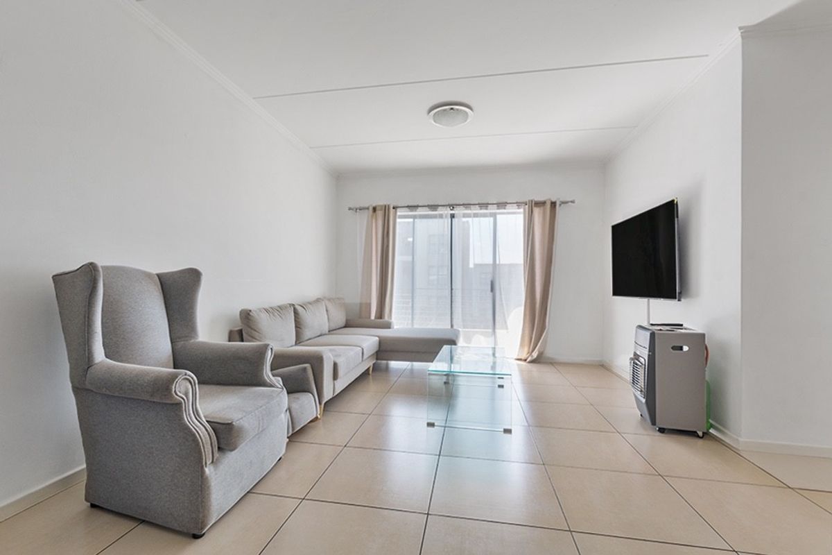 A bright and spacious living room featuring neutral tiled flooring and a sliding glass door providing access to the outdoor area.