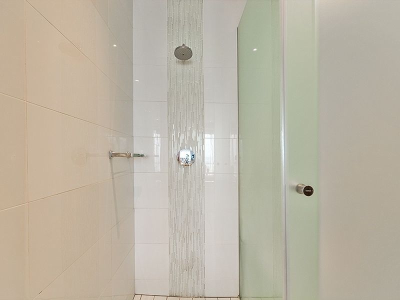 A modern walk-in shower featuring a rainfall shower head, mosaic tile accent strip, and a frosted glass shower screen.