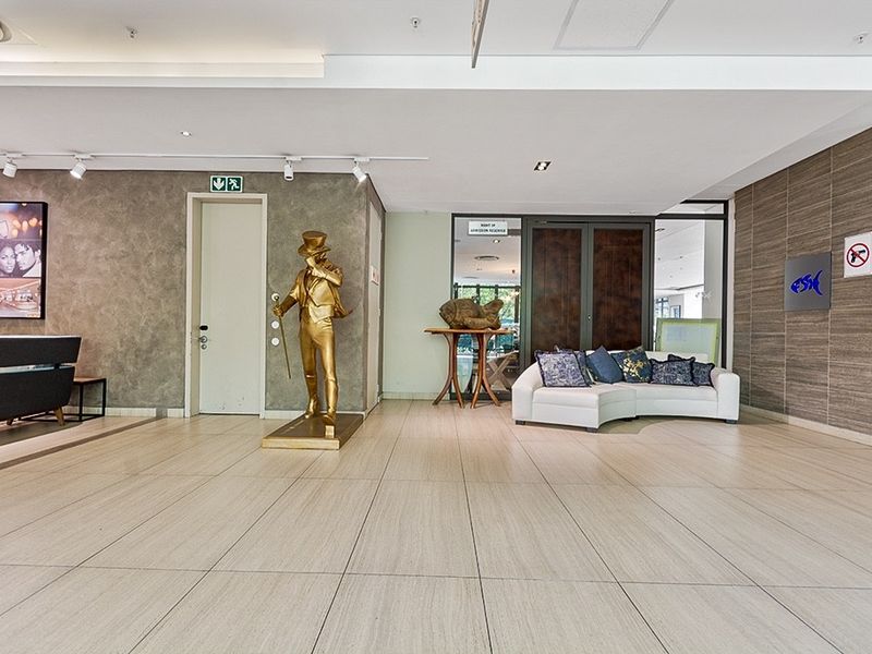 A spacious and modern apartment building entrance lobby featuring tiled flooring, recessed ceiling lighting, and contemporary textured wall finishes.