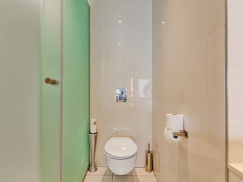 A modern bathroom featuring a wall-mounted toilet with a concealed cistern, complemented by neutral ceramic wall and floor tiles.