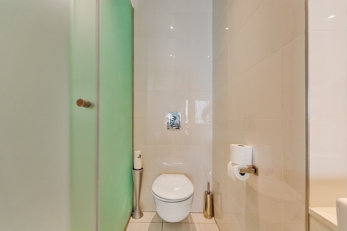 A modern bathroom featuring a wall-mounted toilet with a concealed cistern, complemented by neutral ceramic wall and floor tiles.