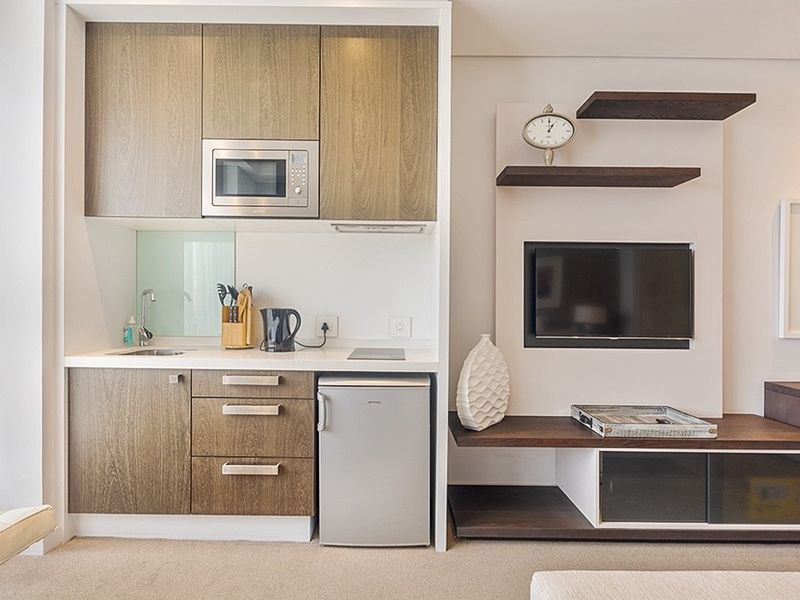 Compact open-plan kitchenette featuring modern wood-grain cabinetry, integrated microwave, and a built-in media console with shelving.