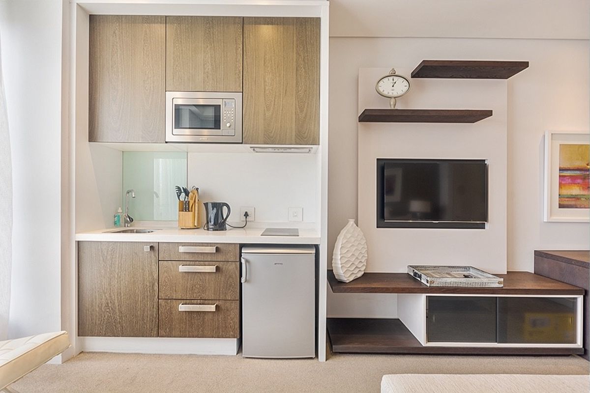 Compact open-plan kitchenette featuring modern wood-grain cabinetry, integrated microwave, and a built-in media console with shelving.