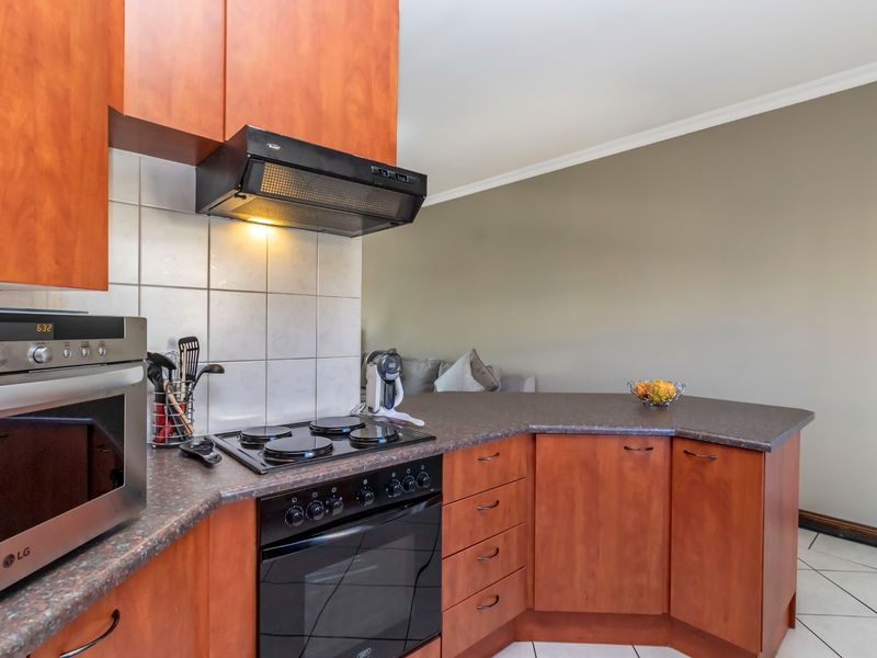 A functional kitchen featuring wood-finish cabinetry, laminate countertops, a built-in oven with hob, and an extractor fan, with tiled flooring throughout.