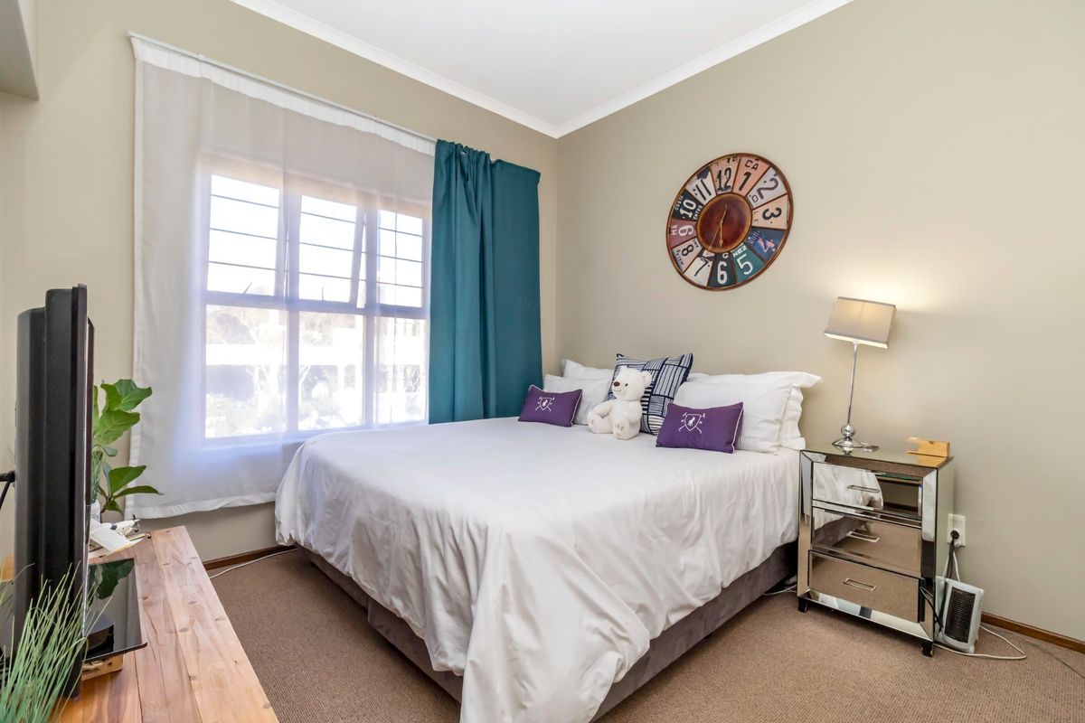 A well-maintained bedroom featuring carpeted flooring, neutral wall tones, and a window fitted with security bars.