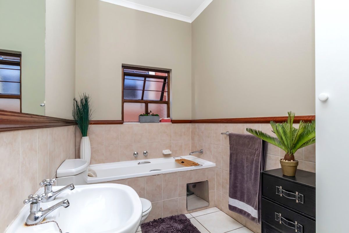 A functional bathroom featuring a bathtub, pedestal basin, and neutral wall tiling with a decorative wooden dado rail.