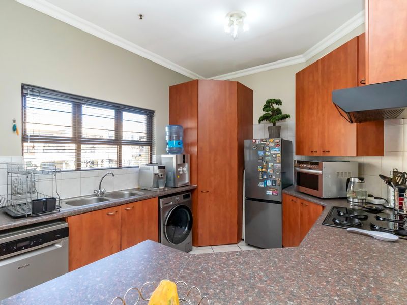 Functional kitchen featuring wood-look cabinetry, laminate countertops, built-in oven, gas hob, extractor fan, and dedicated space for laundry appliances.