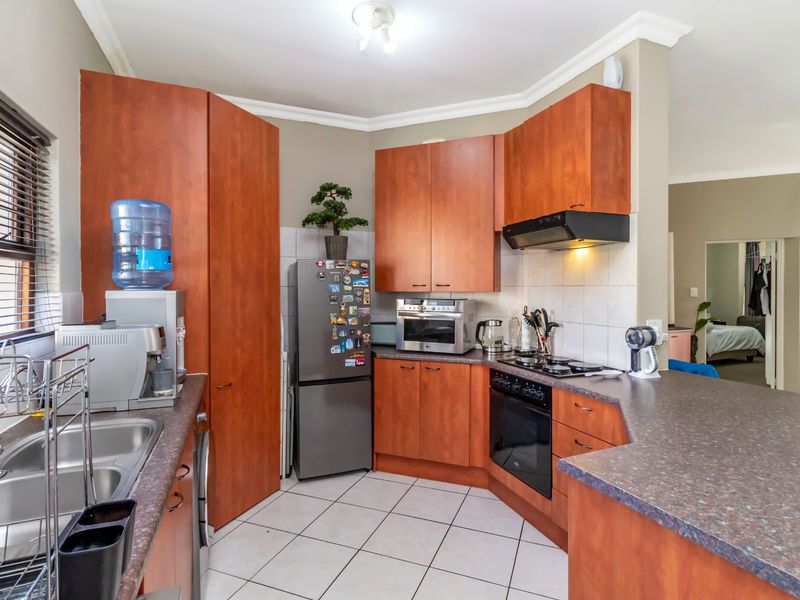 Functional kitchen featuring wood-finish cabinetry, laminate countertops, built-in oven with gas hob, extractor fan, and tiled flooring.