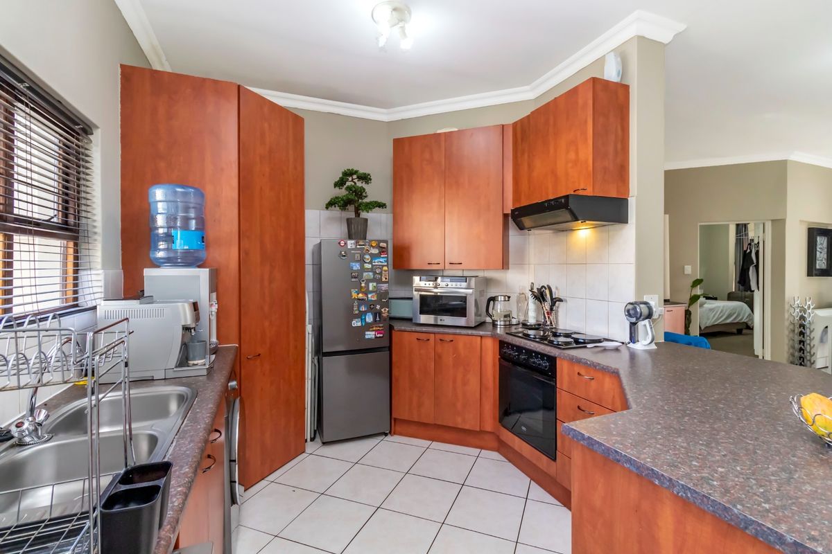 Functional kitchen featuring wood-finish cabinetry, laminate countertops, built-in oven with gas hob, extractor fan, and tiled flooring.