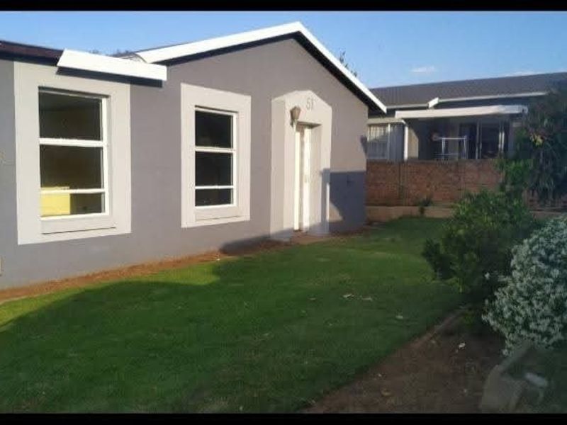 A front view of a single-story residential house featuring a grey painted exterior, aluminium window frames, and a well-maintained front lawn.