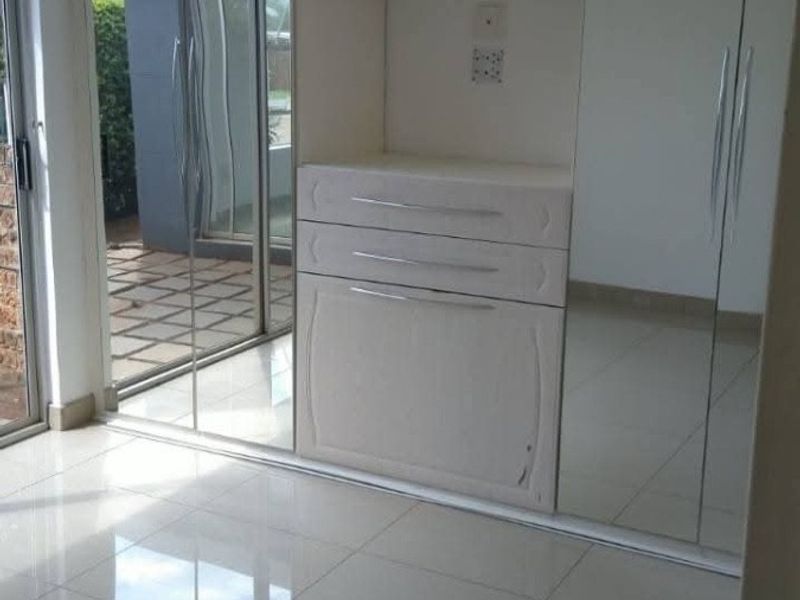 A bright bedroom featuring polished tiled floors, extensive built-in cupboards with mirrored doors, and direct access to an outdoor patio area.